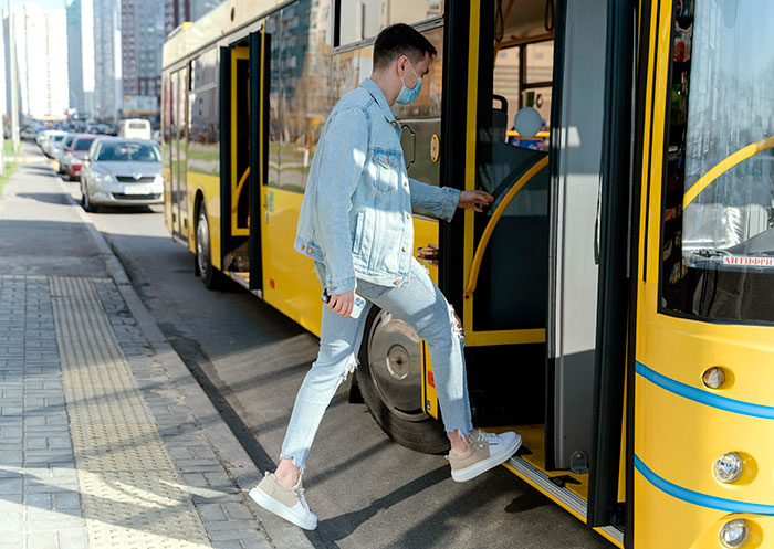 Man wearing denim and a mask boards a yellow bus, showcasing essential knowledge of public transport.