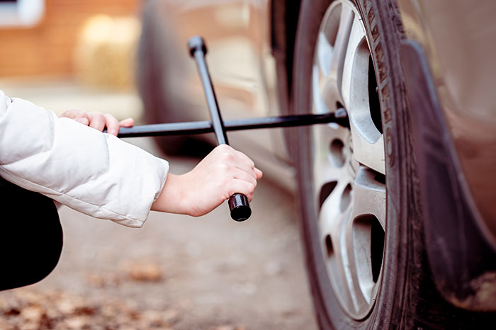 Person using a lug wrench to change a car tire, showcasing essential basic knowledge skills.