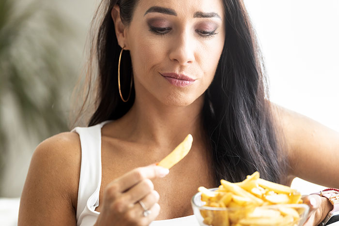 Woman with hoop earrings contemplating fries, considering healthy eating as basic knowledge.