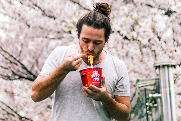Man outdoors eating instant noodles, showcasing basic knowledge of easy food preparation.