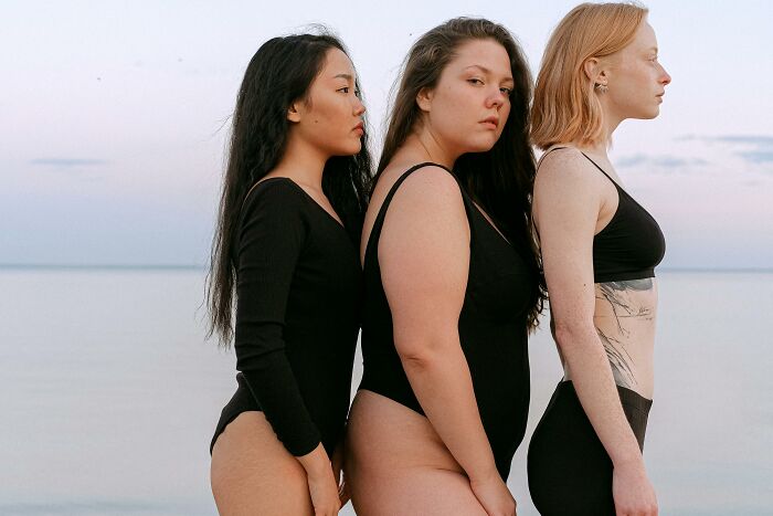 Three women in swimsuits standing side by side on a beach, illustrating diverse beauty standards and trends.