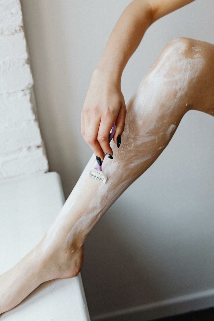 Person shaving leg with foam, highlighting beauty standards and trends.