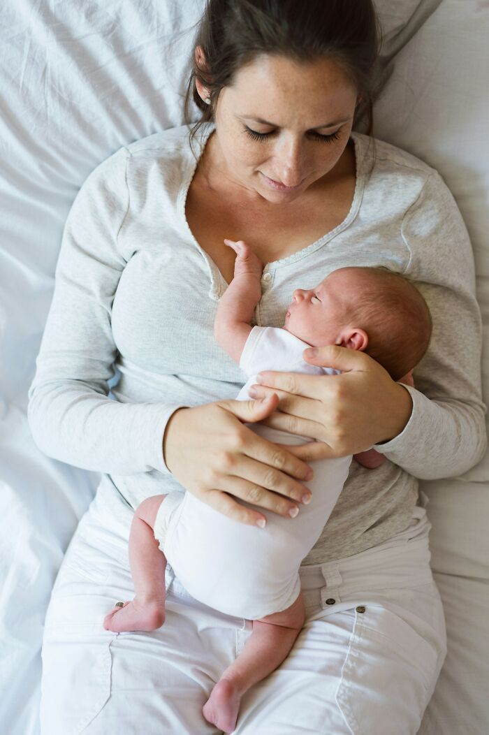 Mother in grey top cradling a newborn on bed, showcasing natural beauty and love.