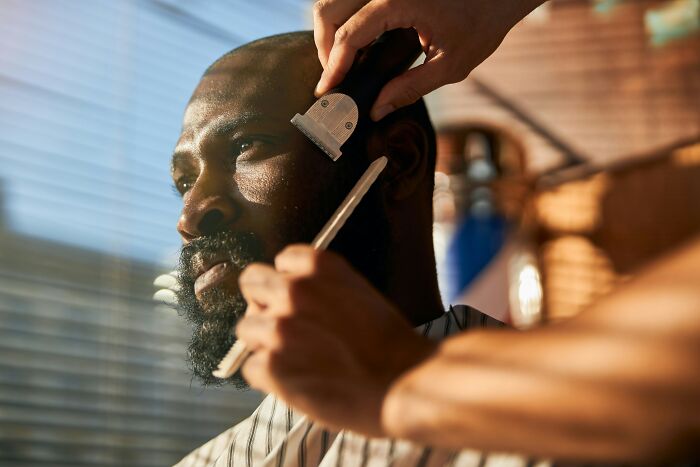 Man receiving a haircut and beard trim, showcasing natural beauty standards in a barber shop setting.