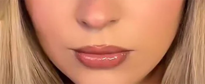 Close-up of a person's lips with glossy makeup, highlighting beauty standards trends.