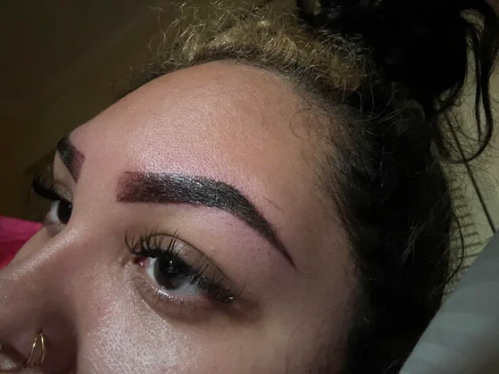 Close-up of a woman's face highlighting bold, unnatural eyebrows, aligned with disliked beauty trends.