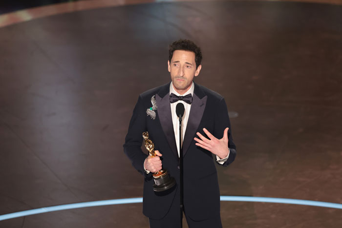 A man in a tuxedo holding an Oscar statue on stage, 2025.