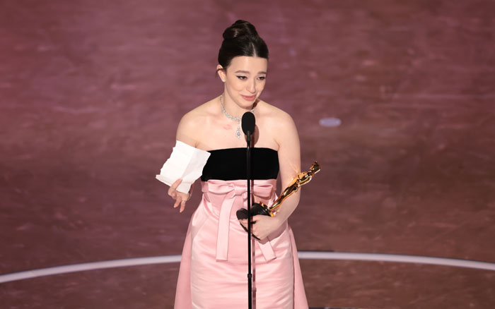 Recipient holding Oscar statuette during the 2025 Oscars ceremony, dressed in a pink and black gown on stage.