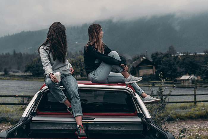 Two friends sitting on a car, enjoying a scenic view, illustrating a best friend's outdoor escape from their living situation.