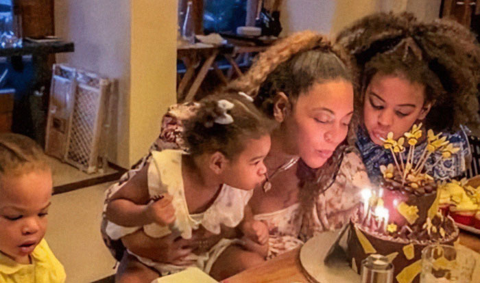 Beyonc&eacute; with her children celebrating a birthday, with a cake and candles on the table.