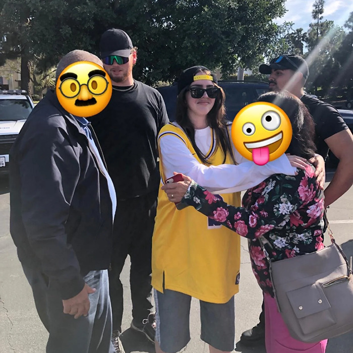 Billie Eilish look-alike in a yellow jersey takes photos with fans at a crowded outdoor event.
