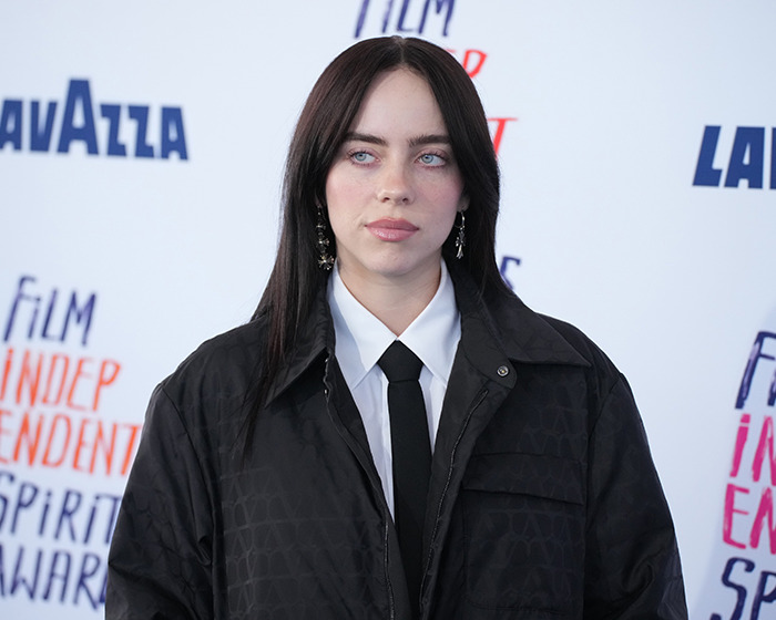 Billie Eilish look-alike in a black jacket and tie at a public event, causing mall chaos despite differing opinions.