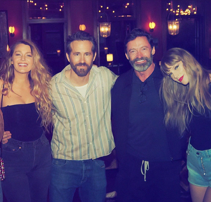 Four people posing closely together in a warmly lit room, featuring Hugh Jackman.