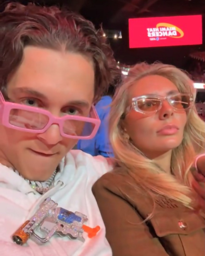 A person with pink glasses and a toy gun, another with sunglasses at an NBA event.