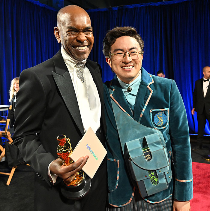 Two men smiling, one holding an Oscar, posing together backstage at Oscars 2025.