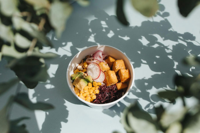 A colorful salad bowl with corn, radishes, and greens, surrounded by leafy shadows, related to cooking.