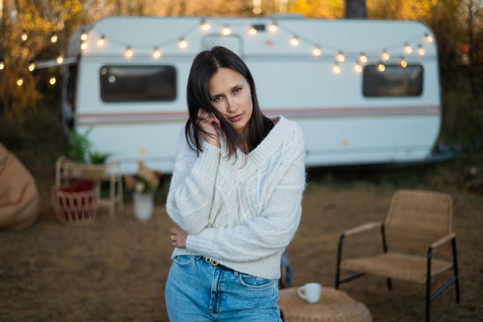 Woman in cozy sweater stands concerned in front of a camper, holding her phone. Woman in cozy sweater stands concerned in front of a camper, holding her phone.