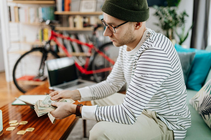 Man in striped shirt counting money, surrounded by toys; reflects financial behavior issues and relationship tension.