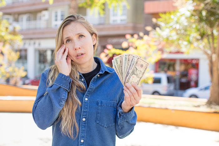 Woman outside holding cash, looking frustrated, emphasizing relationship and financial issues.