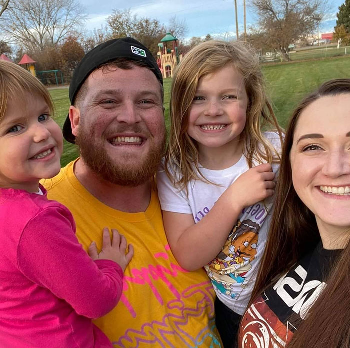 A smiling family of four at a park on a sunny day, with the daughters in colorful outfits. A smiling family of four at a park on a sunny day, with the daughters in colorful outfits.