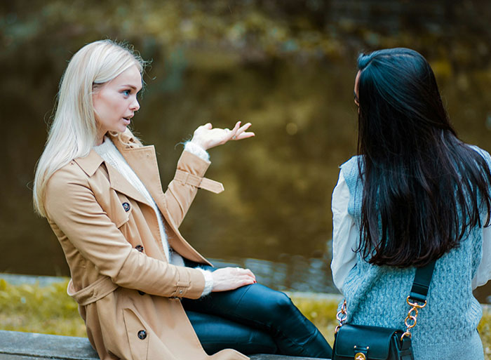 Two women engaged in a serious conversation by a lake, highlighting a bridesmaid discussing a controversial request. Two women engaged in a serious conversation by a lake, highlighting a bridesmaid discussing a controversial request.