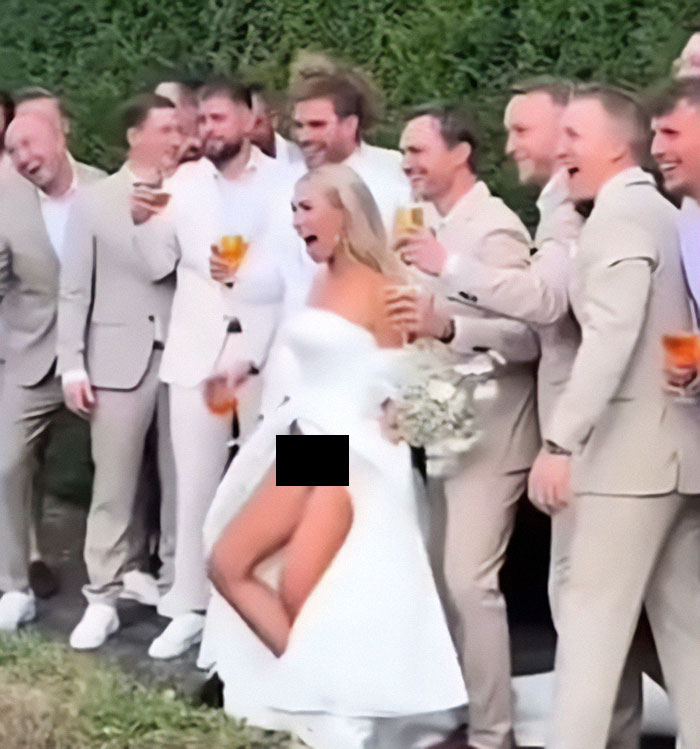 Bride flashes underwear during photoshoot with groomsmen laughing, capturing a quirky wedding moment.