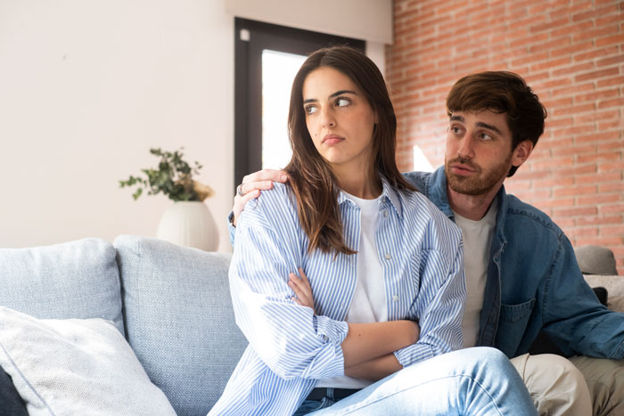 Woman looking away, sitting on a sofa with man, discussing immigration issues.