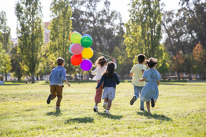 Children running with balloons in a park, symbolizing escape and freedom related to a babysitting nightmare.