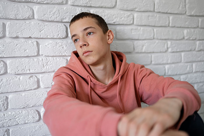 Teenager in casual wear sits pensively against a white brick wall, related to babysitting nightmare incident.