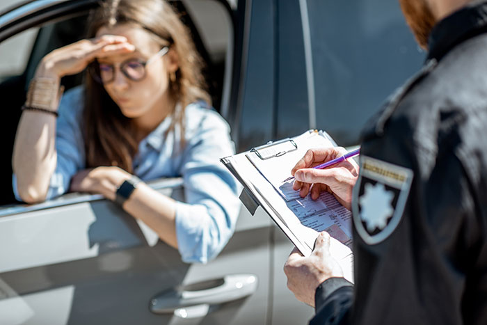 A woman in a car looks distressed as a police officer writes a ticket.
