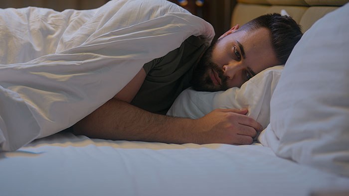 A man lying in bed, appearing pensive, related to brother's unusual +1 choice at a wedding.