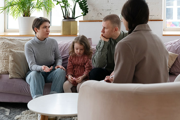 Woman conversing with a couple and a child in a living room, discussing an unexpected visit. Woman conversing with a couple and a child in a living room, discussing an unexpected visit.