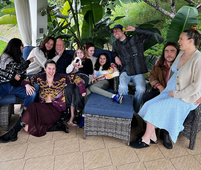 A group of people, including Bruce Willis, sitting on outdoor furniture surrounded by lush plants. A group of people, including Bruce Willis, sitting on outdoor furniture surrounded by lush plants.
