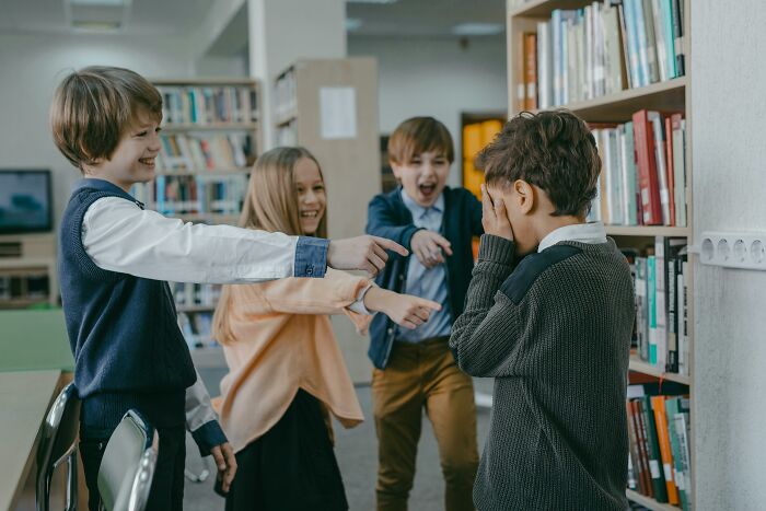 Children bullying a peer in the library over something trivial, pointing and laughing.