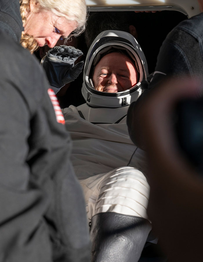 Astronaut in space suit smiling inside capsule, highlighting effects of 9-month space mission.