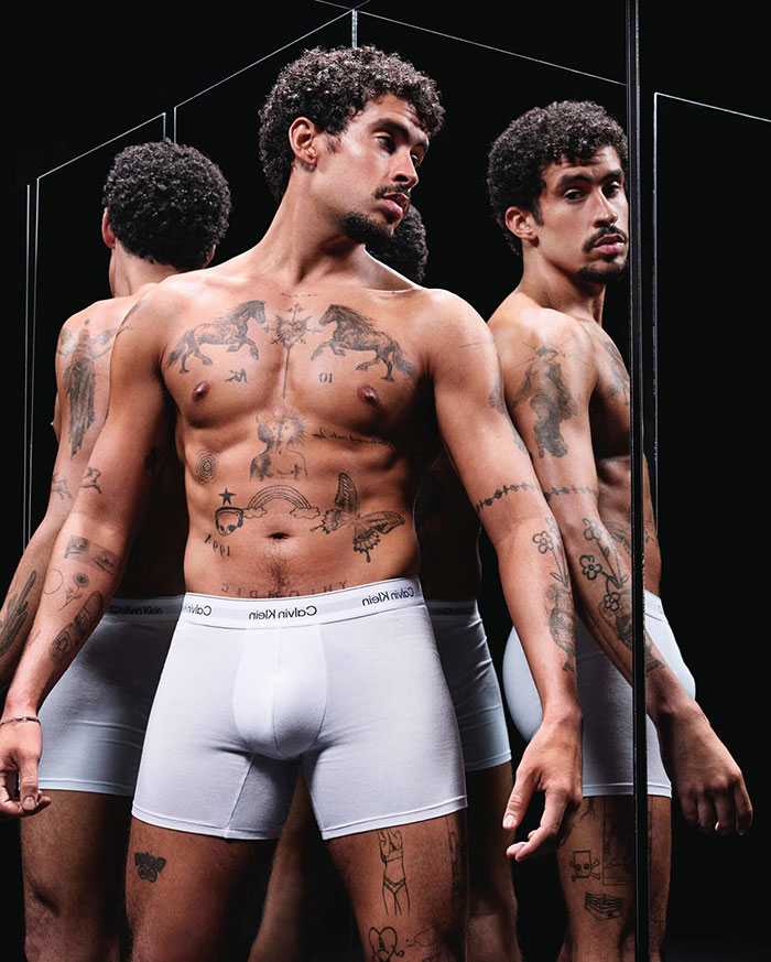 Man posing in Calvin Klein underwear, showcasing tattoos and reflection in a mirror, highlighting a viral campaign feature.