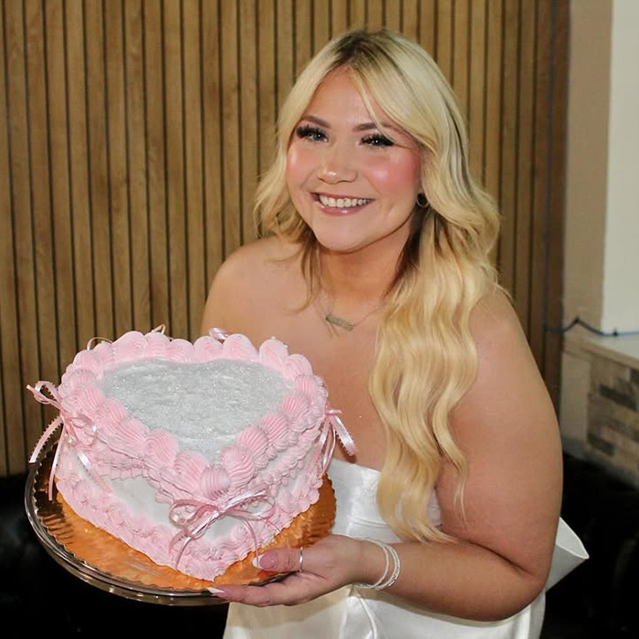 Young woman holding a heart-shaped cake at her bachelorette party, smiling brightly.