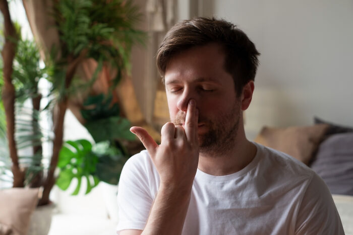 Man in white shirt sitting in a cozy room, touching his face.