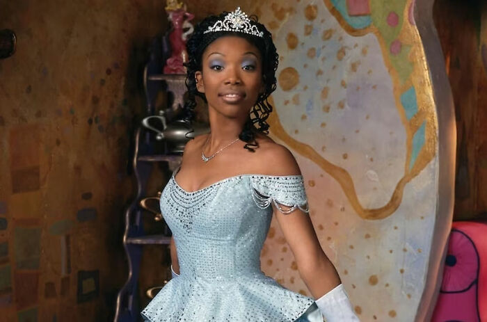 Celebrity in a blue gown and tiara, posing elegantly in a colorful room.