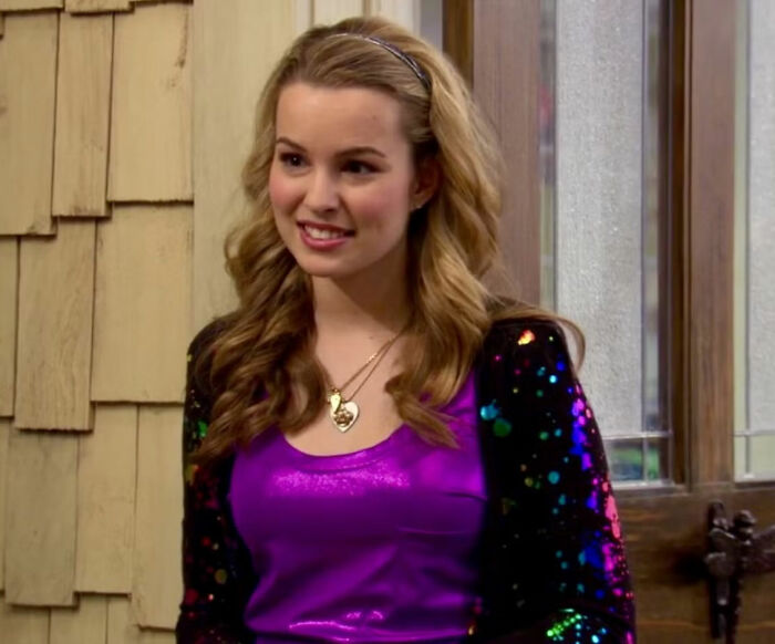 Young woman in a colorful outfit, representing a celeb seemingly disappeared from the media, standing indoors and smiling.