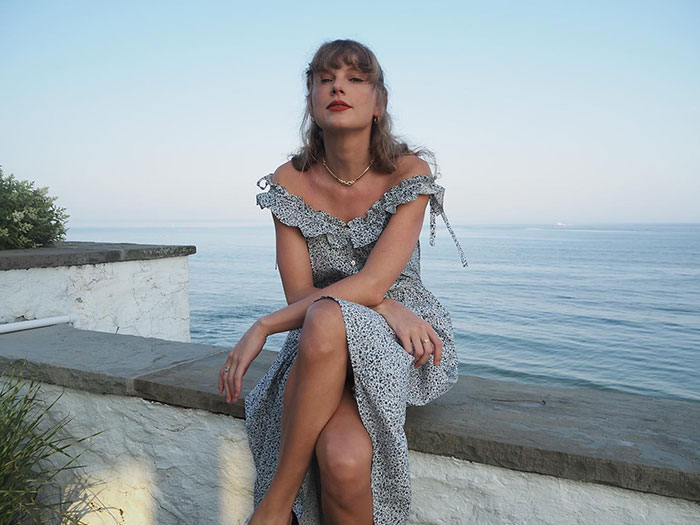 Celebrity in a patterned dress seated by the sea, exuding class and poise.