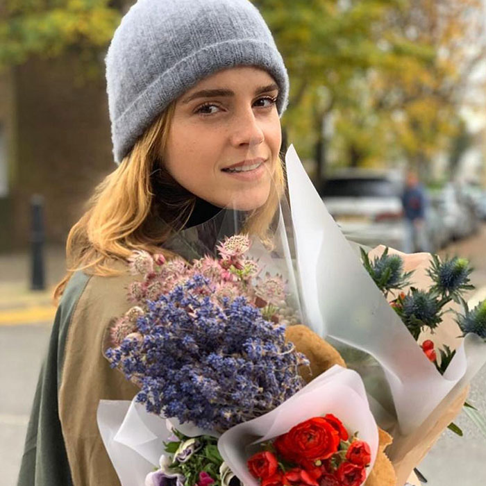 Celebrity holding colorful flowers, wearing a gray beanie.