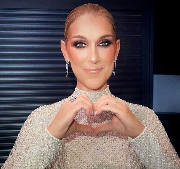 Céline Dion making a heart shape with her hands, wearing a sparkling outfit, smiling directly at the camera. Céline Dion making a heart shape with her hands, wearing a sparkling outfit, smiling directly at the camera.
