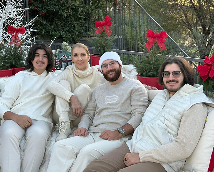 Céline Dion with her twin sons, all dressed in winter attire, sitting outdoors surrounded by festive decorations. Céline Dion with her twin sons, all dressed in winter attire, sitting outdoors surrounded by festive decorations.
