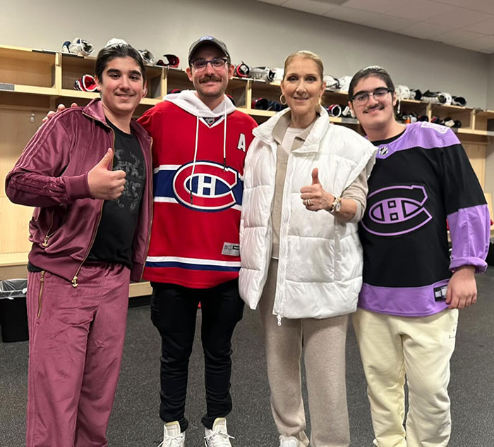Céline Dion with bearded twin sons in a casual setting, posing together in a sports-themed room. Céline Dion with bearded twin sons in a casual setting, posing together in a sports-themed room.