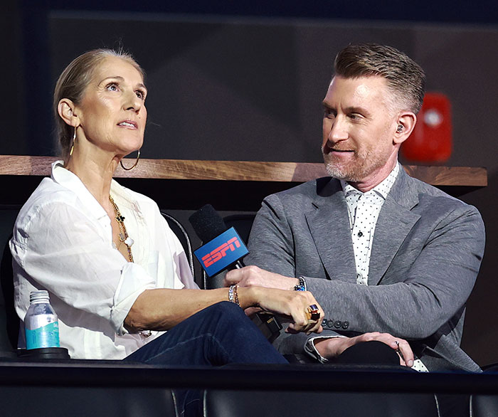 Céline Dion holding an ESPN microphone, sitting with a man, both dressed in casual attire. Céline Dion holding an ESPN microphone, sitting with a man, both dressed in casual attire.