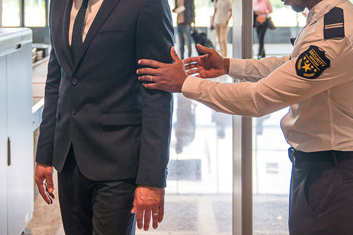 Security officer patting down a worker in a suit at a checkpoint, highlighting compliance with workplace rules.