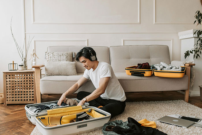 Man packing suitcase in living room, wearing headphones, while seated on a beige carpet. Man packing suitcase in living room, wearing headphones, while seated on a beige carpet.