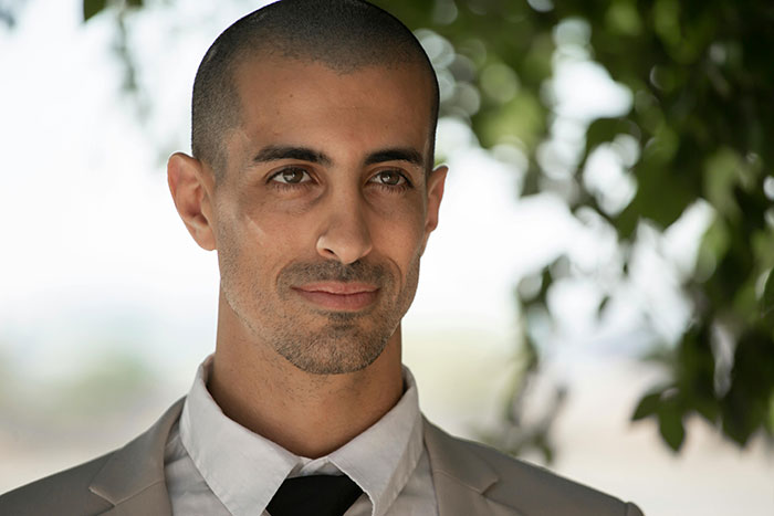 Man outdoors in a light suit, looking contemplative, with trees in the background, representing affair partners narrative.