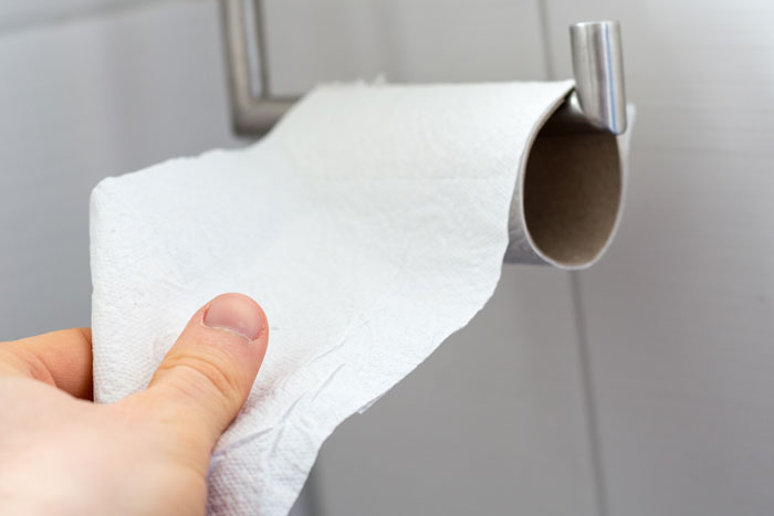 Toilet paper roll in restroom highlighted for hidden needle marks warning.